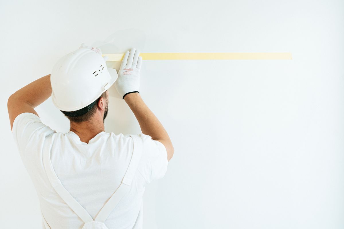 Maler klebt eine weiße Wand mit Kreppband ab — Beispielfoto